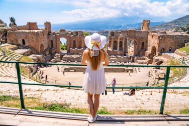 Jule 04, 2018. Taormina, İtalya. Güzel kız uzun beyaz elbise ve beyaz yaz şapka, antik Yunan tiyatro Taormina İtalya kazanı.