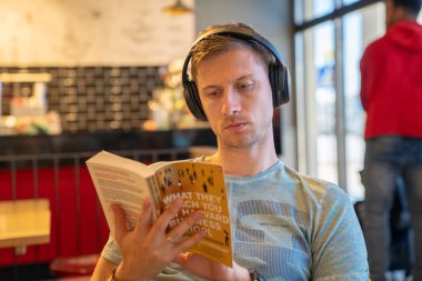 20 Haziran 2018. Valletta, Malta. Harvard hakkında bir kitap okuma kulaklık ile kafede oturan genç adam.