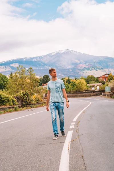 May 20, 2010. Sicily, Italy. View on the eruption Etna volcano from the lonely road. Young man walking down the road with eruption on the background.