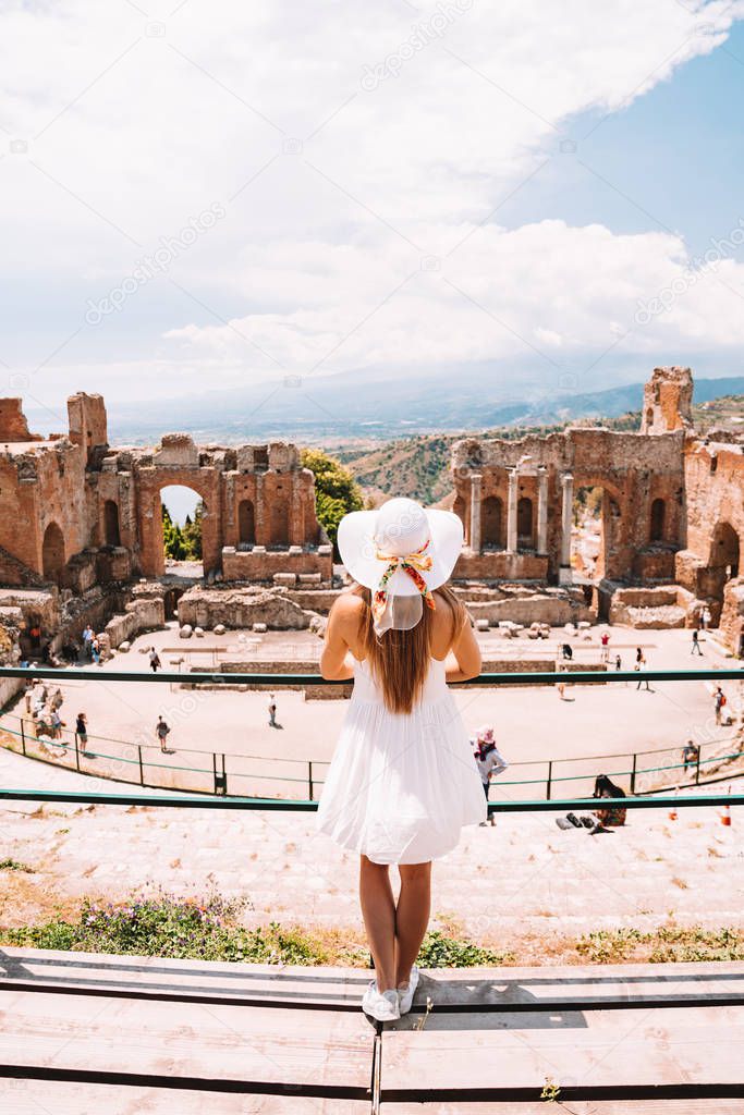 Jule 04, 2018. Taormina, Italy. Beautiful girl in a long white dress and white summer hat at the caldron of the ancient Greek Theater of Taormina in Italy.
