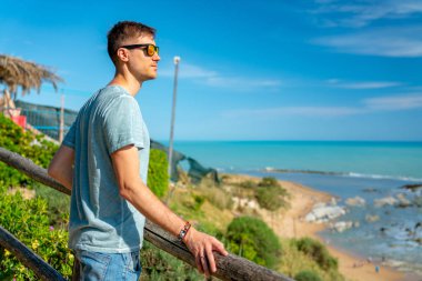 20 Haziran 2018. Sicilya, İtalya. Güneş gözlüğü takıyor ve güzel güneşli gün boyunca Akdeniz deniz kıyısında genç adam. 