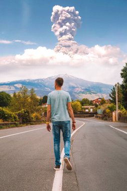 May 20, 2010. Sicily, Italy. View on the eruption Etna volcano from the lonely road. Young man walking down the road with eruption on the background. clipart