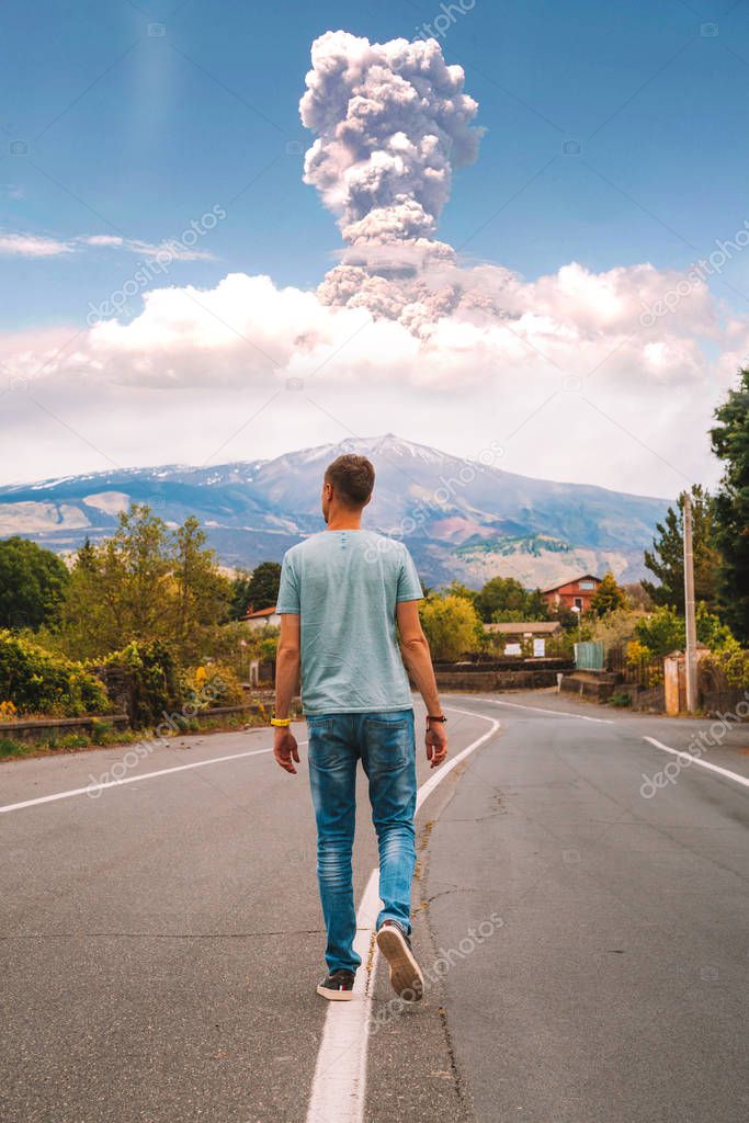 May 20, 2010. Sicily, Italy. View on the eruption Etna volcano from the lonely road. Young man walking down the road with eruption on the background.