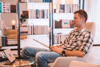 Saalbach, Avusturya. Alpina hotel. 20 Mart 2018. Büyük windows yakınındaki bir rahat Kütüphane odada bir sandalyede oturan genç adam.