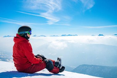 Genç adam - bulutlar üzerinde manzaranın dağın tepesinde oturan snowboard. Bulutların üzerinde oturuyor. Güzel kış doğa dağlarda.
