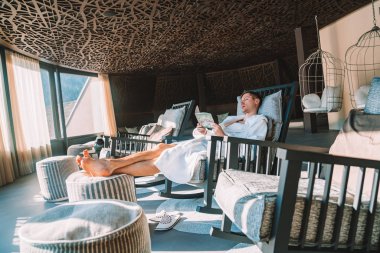 Genç adam kış süre içinde inanılmaz bir dağ manzaralı spa açık bir teras üzerinde tüyler ürpertici bir elbise içinde. Kayak Merkezi.