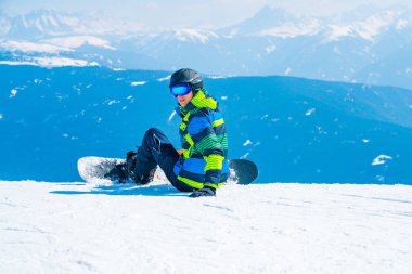 Saalbach, Avusturya. 20 Mart 2018. Genç adamla ufuk içine izlerken Alpleri'nde dağın tepesinde oturan bir snowboard. Kayak Merkezi hayran. Snowboard.