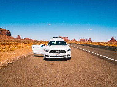30 Temmuz 2018. Anıt Vadisi Milli Parkı, Utah, Amerika Birleşik Devletleri. Beyaz Ford Mustang çölün sonsuz yolda şaşırtıcı bir görünümü olan Anıt Vadisi Milli Parkı, yol kenarında park etmiş.