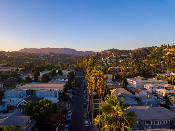 比佛利山庄街与棕榈树在日落在洛杉矶与好莱坞标志在地平线上 — 图库照片