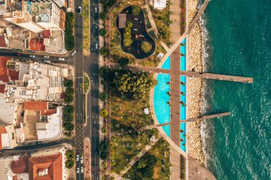 Aerial view of Molos Promenade park on coast of Limassol city centre in Cyprus. Bird's eye view of the jetty, beachfront walk path and palm trees by the sea.