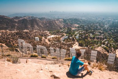 10 Haziran 2018. Los Angeles, Amerika Birleşik Devletleri. La şehir merkezinde Hollywood yazısını arkasından hayran Hollywood hills üstüne oturan genç adam.