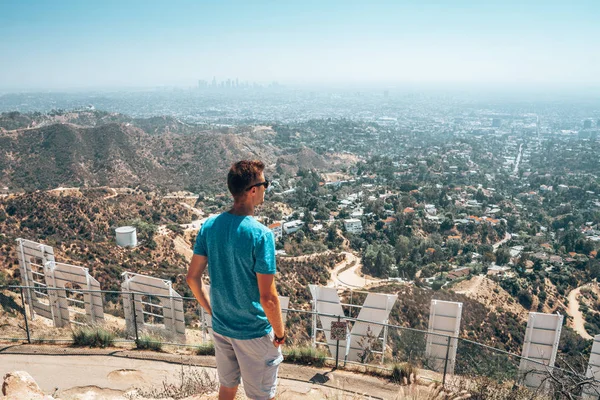 2018 ロサンゼルス アメリカ合衆国 若い男ハリウッド サインの後ろからダウンタウン を眺めハリウッドの丘の上に座っています — ストック写真