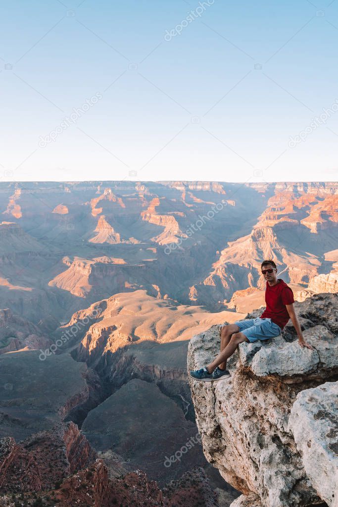 Young man sitting on the edge of the Grand Canyon in USA watching sunset. 