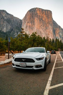 Yosemite National Park, USA. September 10, 2018. Beautiful white Ford Mustang GT parked in the heart of the Yosemite National park with amazing half dome cliffs around it. clipart