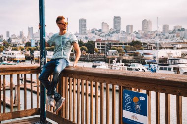 San Francisco, Amerika Birleşik Devletleri. 10 Mayıs 2018. Deniz Aslanları yukarıdan hayran San Francisco'da pier 39, yakınındaki bir muhteşem şehir manzaralı oturan genç adam. 