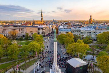 Letonya Milda - Özgürlük heykeli tarafından Riga üzerinde güzel günbatımı görünümü. Özgürlük anıtı. Konser için anıtın etrafında toplanan insanlar. 