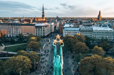 Letonya Milda - Özgürlük heykeli tarafından Riga üzerinde güzel günbatımı görünümü. Özgürlük anıtı. Konser için anıtın etrafında toplanan insanlar. 