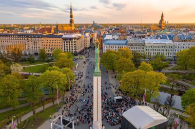 Letonya Milda - Özgürlük heykeli tarafından Riga üzerinde güzel günbatımı görünümü. Özgürlük anıtı. Konser için anıtın etrafında toplanan insanlar. 