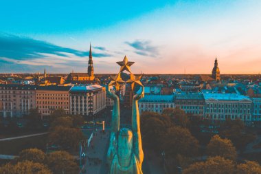 Letonya Milda - Özgürlük heykeli tarafından Riga üzerinde güzel günbatımı görünümü. Özgürlük anıtı. Konser için anıtın etrafında toplanan insanlar.  
