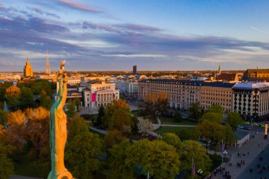 Letonya Milda - Özgürlük heykeli tarafından Riga üzerinde güzel günbatımı görünümü. Özgürlük anıtı. Konser için anıtın etrafında toplanan insanlar.  