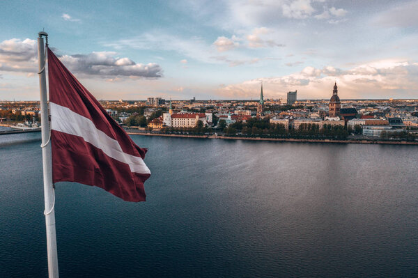 Aerial panorama of Riga city with a big Latvian flag in the foreground. Golden hour.