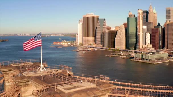 日当たりの良い朝のアメリカ国旗 ニューヨーク市マンハッタン島を背景にブルックリン橋の上に — ストック動画