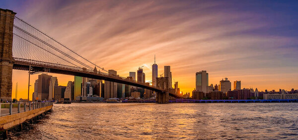 Magical evening sunset view of the Brooklyn bridge from the Brooklyn park with a lower Manhattan view on the other side of the Hudson river.