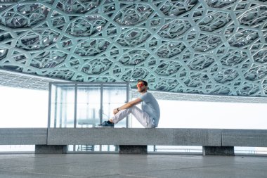 Abu Dabi, Birleşik Arap Emirlikleri, 20 Mayıs 2020: Abu Dabi 'de Louvre' da oturan genç adam sanatını araştırıyor..