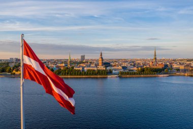 Huge Latvian flag flutters on wind with Riga old town in the background in Latvia. Patriotic video. clipart