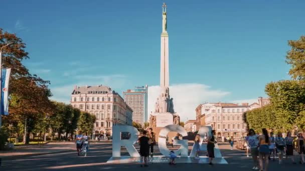 Riga, Lettland. 5. August 2020. Zeitraffer-Ansicht der Menschen, die am Freiheitsdenkmal Milda vorbeirauschen und in der Nähe des riesigen Rigaer Schildes fotografieren.