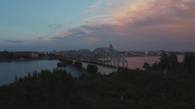  Letonya 'nın başkenti Riga' daki Daugava nehri boyunca uzanan tren demir köprüsünün panoramik videosu..