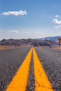 Nevada 'nın kurak çölü boyunca uzanan, uçsuz bucaksız iki şeritli uçsuz bucaksız bir yol engebeli tepeler, uzak dağlar ve minimum bitki örtüsü ile çevrili..