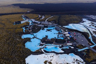 Blue Lagoon Spa 'nın sütlü mavi jeotermal havuzları, oteli ve tesisleri karanlık lav tarlalarıyla çevrili ve yollar kısmen lav tarafından ele geçirilmiş durumda..
