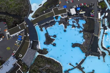 Parlak mavi suları, modern tesisleri ve karanlık lav tarlalarıyla çevrili yolları olan jeotermal kaplıca. Lav akıntısı yakındaki yollara nüfuz ediyor.