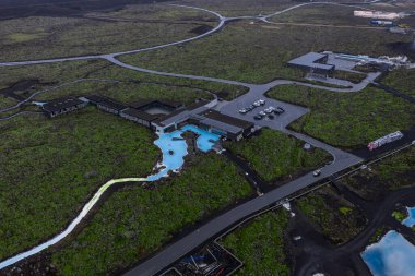 Blue Lagoon Spa 'nın sütlü mavi havuzları, yakındaki otel tesisleri ve yolları kısmen lav akıntıları tarafından işgal edilen koyu lav tarlalarıyla tezat oluşturuyor..