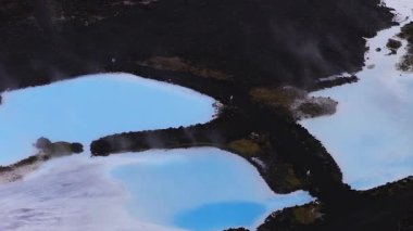İzlanda 'daki Mavi Göl Kaplıcaları' nın hava manzarası, parlak mavi jeotermal sular, siyah lav tarlaları, yükselen buhar ve arazi üzerinde yavaş bir tava..