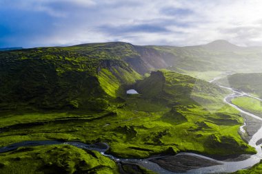 Yeşil yosun kaplı tepeler, göl gibi bir krater, kıvrılan nehirler ve İzlanda 'da parçalı bulutlu bir gökyüzünün altındaki uzak dağlar..