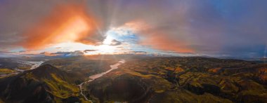 Tepeler, göller ve turuncu, pembe ve mavi gökyüzünün altında kıvrımlı bir nehirle çevrili İzlanda kraterinin hava görüntüsü..
