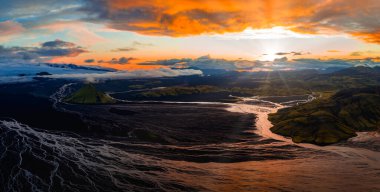 Gün batımında İzlanda 'nın havadan görünüşü, buzullarla örülmüş nehirler, karanlık volkanik arazi ve turuncu ve pembe gökyüzünün altında yeşil bir volkanik krater..