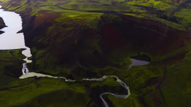İzlanda 'daki yeşil volkanik bir arazinin havadan görünüşü bir krater, kıvrımlı bir nehir, çağlayan bir şelale ve hareketli bir göl..