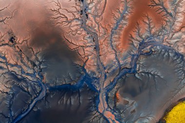 İzlanda 'da parlak sarı bir yama ve görülebilir volkanik oluşumlarla kırmızımsı kahverengi bölgede zikzak çizen mavi akıntıların hava görüntüsü.