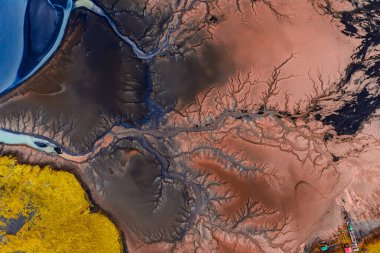 İzlanda 'nın hava görüntüleri, sol üst köşede dallanan nehir kanallarını, kırmızı ve siyah tortuyu, sarı yosunu ve mavi gölü gösteriyor..