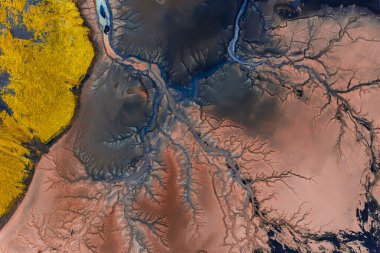Kırmızı ve kahverengi tonlar, sarı yosun ve karanlık volkanik toprak karmaşık desenler oluşturarak İzlanda 'daki kıvrımlı akarsuların ve nehirlerin hava görüntüsü..