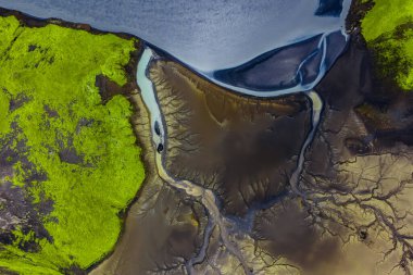 İzlanda 'nın yeşil yosun örtülü arazisinin hava görüntüsü, karanlık volkanik toprak, ve akarsu desenleri olan dingin bir göle doğru akan soluk bir nehir..