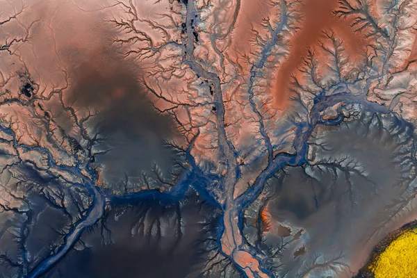 İzlanda 'da parlak sarı bir yama ve görülebilir volkanik oluşumlarla kırmızımsı kahverengi bölgede zikzak çizen mavi akıntıların hava görüntüsü.