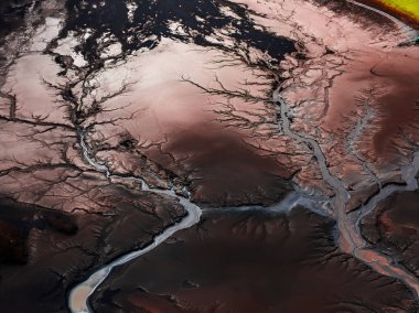 İzlanda 'nın kırmızı kahverengi arazisindeki karışık nehir desenlerinin hava görüntüsü, volkanik toprak, tortu birikintileri ve köşede yeşil bitki örtüsü..