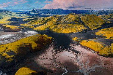 İzlanda 'nın volkanik arazisinin yosun kaplı tepeleri, kıvrımlı dereleri, kırmızı kahverengi tortusu, siyah kumları ve uzak sıradağlarıyla hava manzarası..