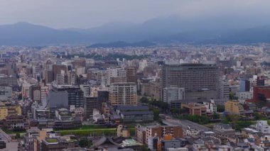 Modern ve geleneksel binaların, tapınak çatılarının ve bulutlu bir gökyüzünün altındaki uzak dağların karışımını gösteren Kyoto, Japonya 'nın hava manzarası..