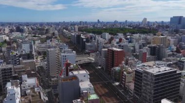 Tokyo, Japonya 'nın hava manzarası, Tokyo Skytree, modern binalar, tren yolları, yeşil bir park, ve geniş bir kamera hareketi..