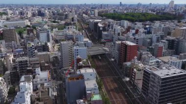Tokyo 'nun havadan görünüşü, yüksek binalar, daha küçük yapılar, hareket eden trenleri olan bir demiryolu ve arka planda yeşil bir park gösteriyor..